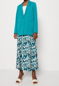 Tyrkysové sako s jedním knoflíkem, doplněné splývavou midi sukní s modro-bílým květinovým vzorem. Nosit s béžovými sandály na podpatku.