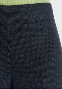 Pantalons ajustés bleu foncé avec un tissu texturé, présentant une taille plate et un motif tissé subtil.