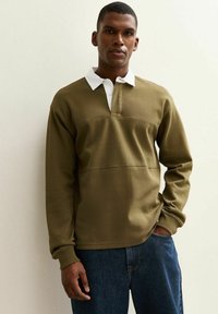 Olive green sweatshirt with a white collared neckline, featuring a half-button placket and textured fabric, paired with blue denim jeans.