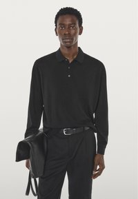Zwart poloshirt met lange mouwen met twee knopen en een zachte textuur, gecombineerd met een zwarte broek en een leren tas. Eenvoudig en elegant design.