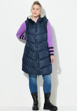 Marineblauwe gewatteerde vest met capuchon, voorzien van een ritssluiting aan de voorkant, chevron-quilting en zijzakken. Aangevuld met een zachte, lichtgekleurde voering.