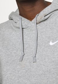Felpa grigia con finitura testurizzata, dotata di tasca frontale, cordini e un piccolo logo Nike bianco sul petto.