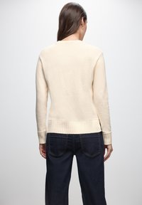 Maglione a maglia crema con orlo e polsini a coste, caratterizzato da una vestibilità rilassata e una texture liscia. Abbinato a jeans in denim scuro.