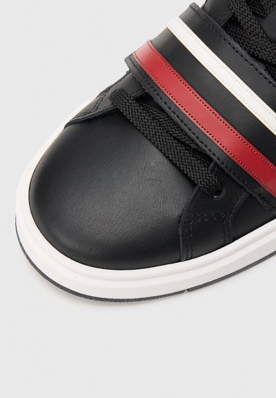 Zapatillas de cuero negras con rayas rojas, blancas y azules, punta redonda, superficie texturizada y suela blanca en contraste. Diseño con cordones.