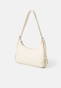 Cream-colored leather handbag with a curved shape, adjustable strap, zippered closure, and subtle side detailing. Smooth texture throughout.