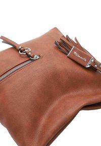 Sac à main en cuir marron avec une surface texturée, équipé d'une fermeture éclair argentée, d'un gland décoratif et d'une étiquette de marque.