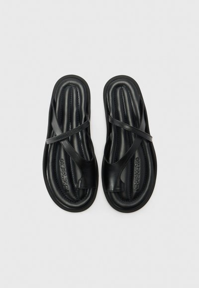 Mustat sandaalit, joissa on teksturoitu, muotoiltu pohja ja ristiin menevä hihnasuunnittelu. Valmistettu sileästä synteettisestä materiaalista, jossa on kohokuvioitu logotieto.