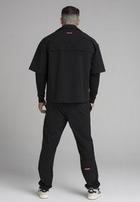 Svart kortärmad skjorta och matchande byxor, med en logotypetikett i röd, tillverkad av ett mjukt tyg med en avslappnad passform.