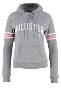 Sudadera gris con capucha, bolsillo delantero, cordón ajustable y texto blanco "Hollister". Presenta rayas rosas y blancas en las mangas.