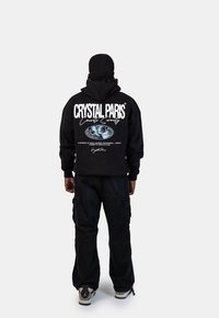 Czarna bluza z kapturem z białym napisem i grafiką z tyłu, w połączeniu z czarnymi spodniami Cargo i szarymi sneakersami.