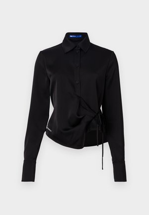 Must musta, pikkade varrukatega särk siledast kangast, nööbitav eesmine osa, ümbritseva disainiga ja külje sidumise detailiga taljes. Omab nööbiga mansette.