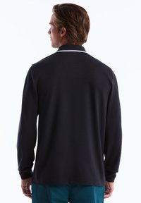 Polo shirt à manches longues navy avec un col à bord blanc, tissu doux, coupe décontractée et manches à poignet, présenté de dos.