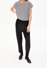 Black, tapered trousers with an elastic waistband paired with a striped, short-sleeved top. Material appears soft and textured.