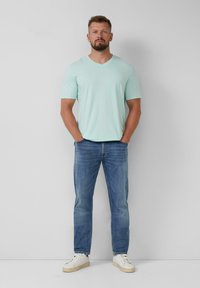 Lichtblauw V-hals T-shirt, denim jeans en witte sneakers. De stof is glad; de jeans hebben een klassieke pasvorm met subtiele vervaging.