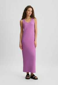 Lang, tætsiddende kjole i en livlig pink nuance, fremstillet af blødt stof. Har en rund halsudskæring og ärmeløs design, parret med sorte sandaler.