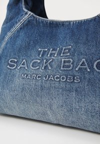 Denim õlakott omab pehmet, kõverat kuju koos nähtavate õmblustega. Tikitud tekstiga on kirjutatud "THE SACK BAG" ja "MARC JACOBS."