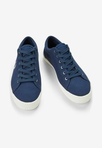 Zapatillas de lona azul marino con punteras redondeadas, suelas de goma blanca y cordones planos. Exterior texturizado con ojales de metal para los cordones.