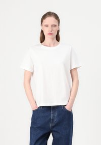 Witte katoenen T-shirt met korte mouwen, ronde hals en een losse fit, gecombineerd met hooggeplaatste blauwe denim jeans. Minimalistisch ontwerp.