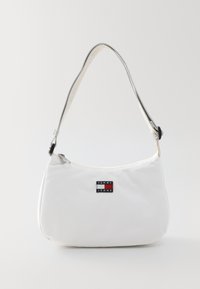 Bolso de hombro de tela blanca con forma redondeada. Presenta una correa plateada y un parche de logo negro con acentos en rojo y azul. Cierre con cremallera.