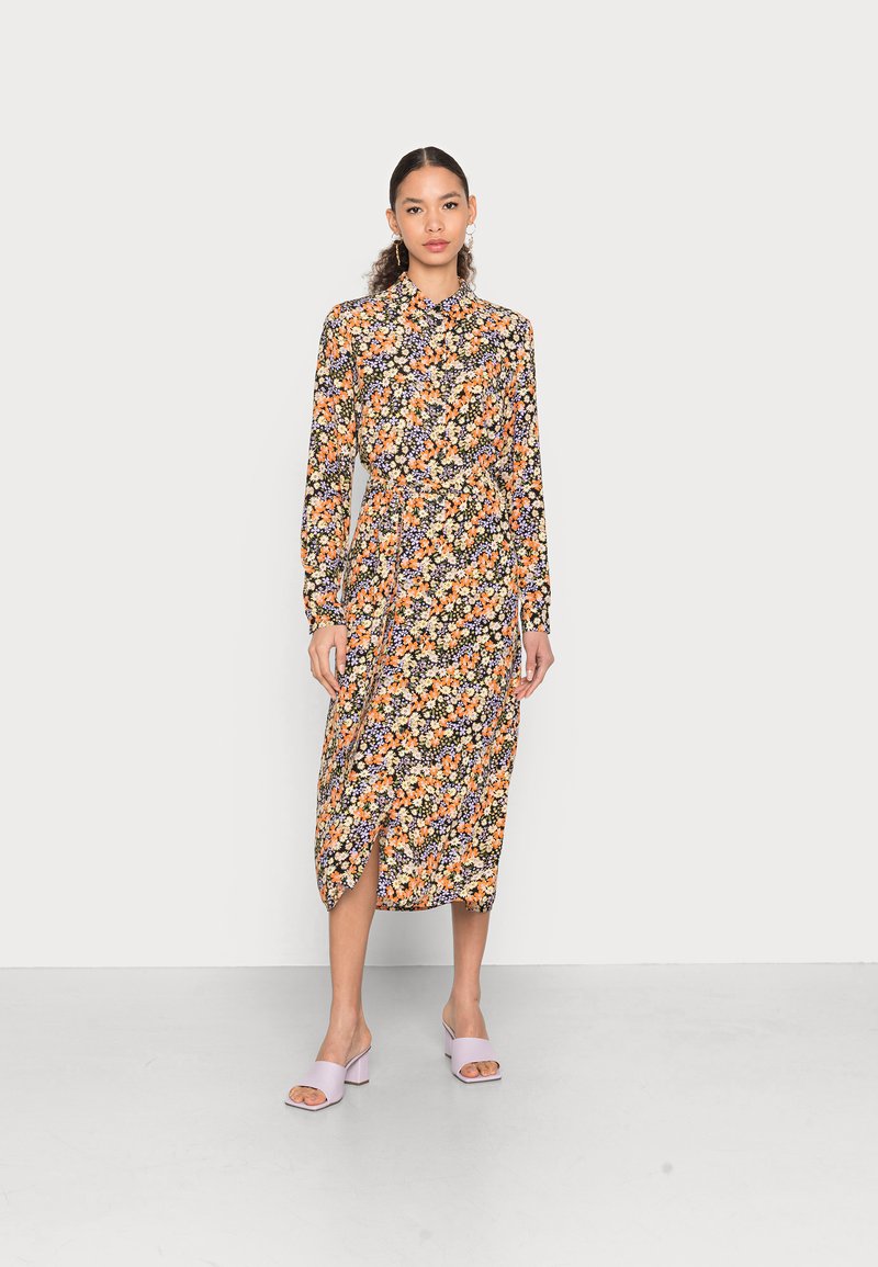 Vestido midi floral com mangas longas, fundo preto, flores laranja e roxas, e fecho de botão. Apresenta uma fenda lateral e cintura cingida.