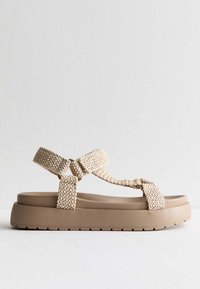 Beige vävda remsandaler med en tjock brun plattformssula. Har en korsdesign och en strukturerad rem för en säker passform.