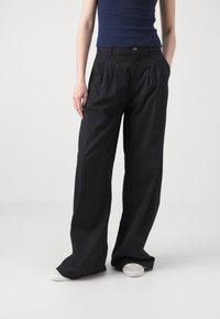 Pantalons larges noirs avec des plis, en tissu léger, dotés de poches latérales et d'une fermeture à bouton sur le devant. Style décontracté.