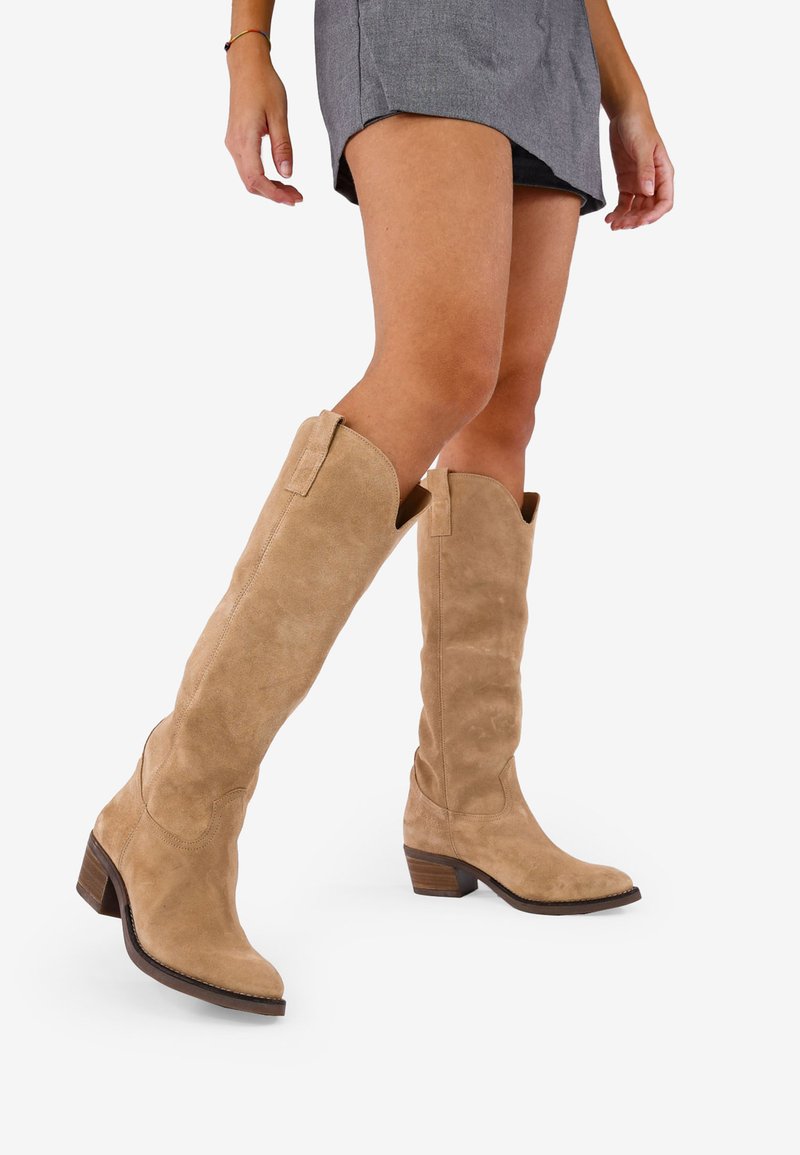 Botas de ante hasta la rodilla en beige claro con punta afilada, tacón de bloque y costuras al estilo western en los laterales. Textura y acabado suaves.