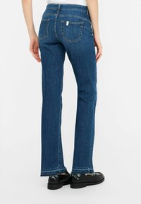 Jeans in denim blu scuro con design a gamba dritta, dotati di due tasche posteriori e orlo sfrangiato. Il materiale sembra resistente con cuciture visibili.
