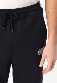 Marineblaue Sweatpants mit elastischem Bund und Kordelzug. Verfügt über ein kleines weißes Logo auf dem Oberschenkel, gefertigt aus weichem Stoff mit glatter Textur.