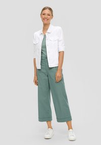 Witte spijkerjasje, groene elastische taillebroek en witte sneakers. Casual fit met opgerolde mouwen en brede broekspijpen.