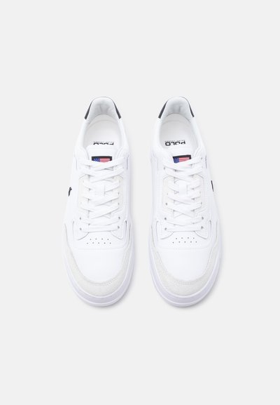 Ζευγάρι λευκών χαμηλών αθλητικών παπουτσιών με κορδόνια, διάτρητα καλύμματα στα δάχτυλα και μικρές πινελιές με την αμερικανική σημαία στη γλώσσα και την ετικέτα της μάρκας μέσα.