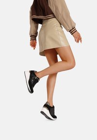Scarpe sportive in bianco e nero con superfici testurizzate, dettagli in metallo e suola spessa, abbinate a una gonna in pelle beige e a una giacca bomber marrone.