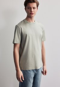 Hellgrünes Baumwoll-T-Shirt mit kurzen Ärmeln, rundem Halsausschnitt und entspannter Passform, kombiniert mit hellblauen Denim-Jeans. Schlichtes Design.