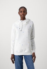 Sudadera blanca con patrones de estrellas coloridas, capucha con cordón y puños acanalados, combinada con jeans azules. Diseño suave y casual, adecuado para superponer.