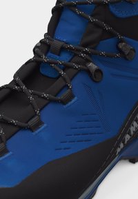 Κοντινή λήψη μπλε και μαύρου ορειβατικού μποτάκι με κορδόνια σε μαύρο και άσπρο μοτίβο και υφασμένες συνθετικές λεπτομέρειες στο επάνω μέρος.