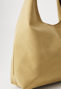 Sac à bandoulière en suède jaune avec une texture douce, une silhouette incurvée et une large ouverture. Détails cousus le long des bords.