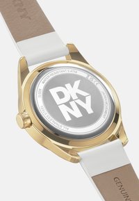 Orologio color oro con quadrante rotondo argentato, cinturino in pelle bianca e cassa dorata. Presenta il logo "DKNY" e resistenza all'acqua fino a 5 ATM.