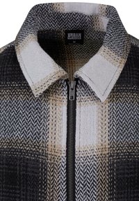 Zbliżenie na czarną, białą i beżową kratkowaną kurtkę z zamkiem z przodu i złożonym kołnierzem, oznaczoną jako Urban Classics rozmiar M.