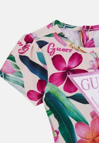 Koszula z krótkim rękawem w kwiatowy wzór, w kolorach różowym i zielonym, z miękkiego materiału, z logo "Guess" w różowym, brokatowym wykończeniu.