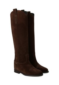 Bottes en suède marron jusqu'au genou avec un bout arrondi, un talon bas et une couture décorative sur le devant. Présente des languettes de tirage sur le dessus.