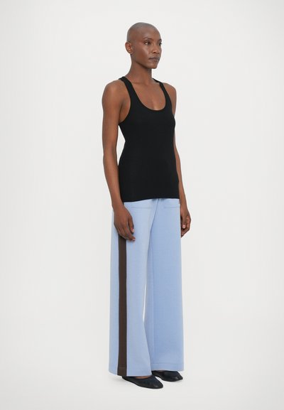 Top sin mangas negro combinado con pantalones de pierna ancha azul claro que presentan una franja lateral marrón oscuro. Tejido suave y corte relajado.