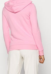 Sudadera con capucha de color rosa claro, hecha de un tejido suave y texturizado. Presenta un bolsillo tipo canguro y puños y dobladillo acanalados para un ajuste seguro.