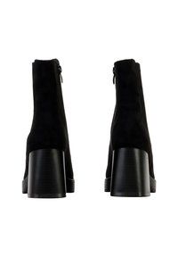 Bottines en daim noir avec un talon bloc, dotées d'une fermeture éclair et d'une texture lisse. Le talon présente un design rainuré.