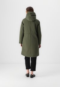 Olīvzaļš parka ar kapuci, sašaurinātu jostasvietu un pogām aizdara, ar gludu, teksturētu audumu un ceļu garumu.