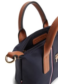 Τσάντα χειρός από ναυτικό ύφασμα με καφέ δερμάτινες λεπτομέρειες, επάνω λαβές, κλείσιμο με φερμουάρ και χρυσό λογότυπο. Διαθέτει αντίθετη λεπτομέρεια με ρίγες.