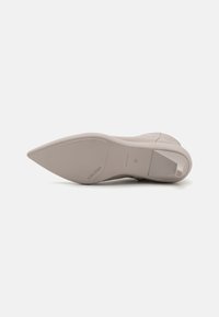 Zapato de tacón alto beige con punta afilada, textura suave y logo grabado en la suela. El diseño presenta una silueta elegante y material duradero.