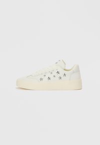 Λευκό αθλητικό παπούτσι με λείο δέρμα στο επάνω μέρος. Διαθέτει ασημένιες διακοσμήσεις σε σχήμα αστέρα και παχύ, υφασμένο πέλμα. Κλείσιμο με κορδόνια.