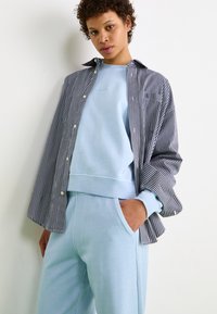 Sweatshirt bleu superposé sous une chemise à rayures noir et blanc, associé à un pantalon de jogging bleu clair. Tissus doux, coupe décontractée.