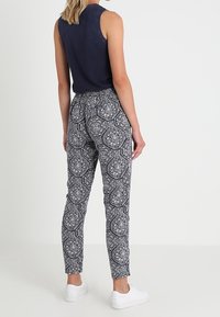 Navy sleeveless top paired with patterned black and white tapered pants featuring an elastic waistband and white sneakers.