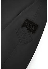 Sort stof med to "POLO CLUB" logoer i tekstureret gummi og stof, placeret på materialets overflade med en mat finish.